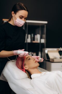 Aesthetician performing microcurrent facial treatment on woman