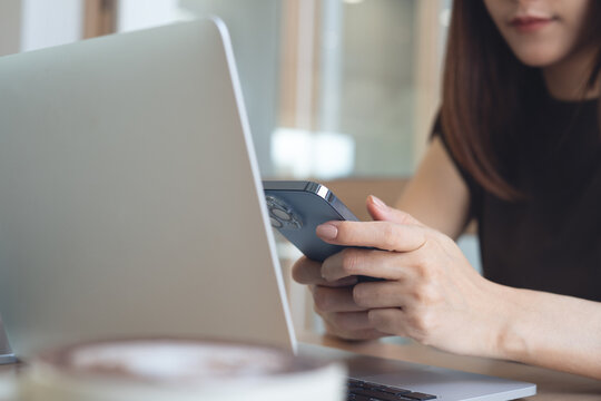 Close up, woman using smartphone while working on laptop, remote working in modern workspace, surfing the net, social media networking