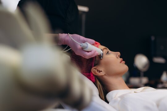 Woman receiving microcurrent facial treatment in clinic