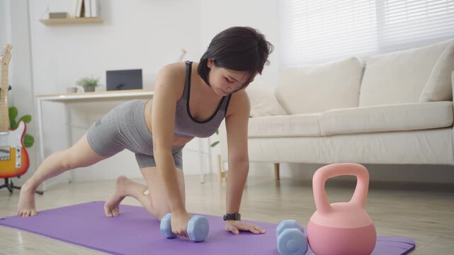 Asian Woman in Sportswear Doing Dumbbell Row Exercise on Yoga Mat in Living Room at Home, Sport concept.