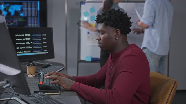 Male developer focuses on coding with AI assistance while monitoring real-time data dashboards and metrics for data-driven development decisions.