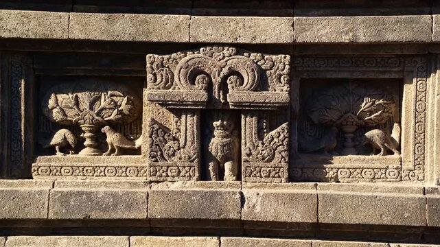 Ancient stone relief panels display carved figures and decorative guardians on the walls of Prambanan Temple in Central Java.