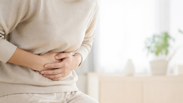 Young woman holding her stomach in pain in the living room representing severe abdominal ache, digestive problems, and menstrual cramps.