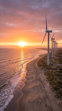 Wind turbines standing along a scenic coastline during a vibrant orange sunset