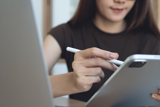 Close up, young asian business woman, freelancer using stylus on digital tablet with laptop on office table. Graphic designer using touchpad on design project