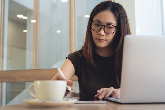 Close up, asian business woman using stylus pen and digital tablet while working on laptop at cafe. Graphic designer, freelancer remote working, using touchpad at coffee shop