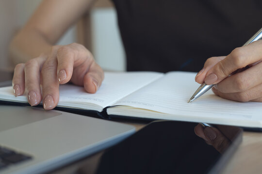 Closeup, business woman writing in notebook for proposal, doing online research using laptop. student studying online class and taking note on notepad, business planning, e-learning