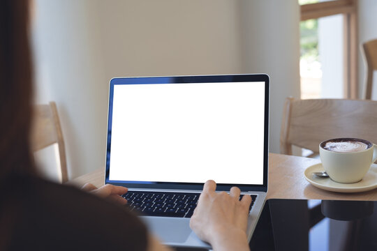 Mockup blank white screen laptop computer. Business woman using and searching the information on laptop with empty screen on wooden table in modern loft cafe. Back view, template for online marketing