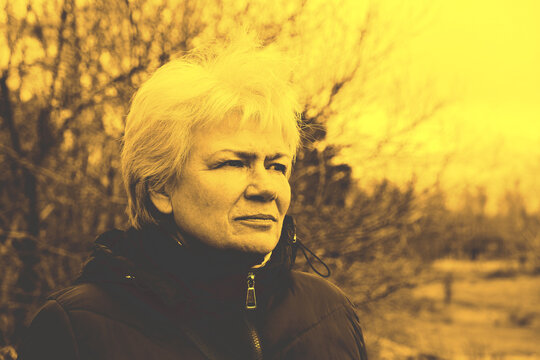 Senior woman outdoors in autumn, pensive, enjoying the peaceful surroundings. High‑contrast vintage toning with an old‑newspaper style aesthetic. Autumn atmosphere, reflective mood, nostalgic look.