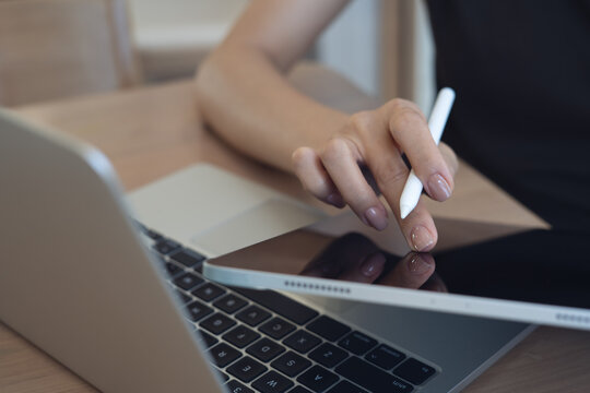 Close up, business woman, using digital tablet, finger touching on tablet screen with laptop on office table. Person reading and proofing e-document, working at office.