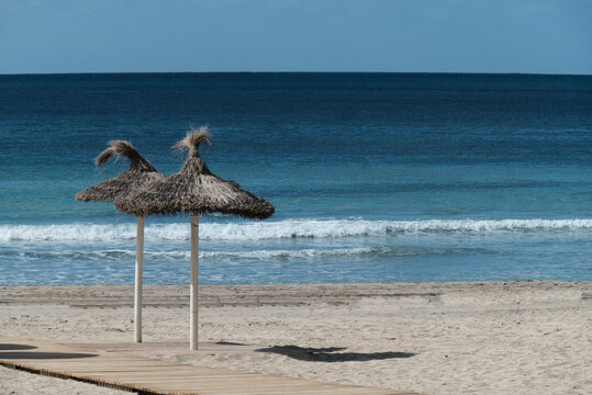 Strand mit Strohsonnenschirmen vor blauem Meer