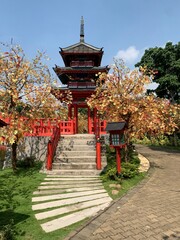 Beautiful three-tiered traditional red pagoda building surrounded by artificial autumn maple trees in a themed public park. © Miftahus