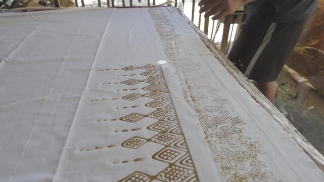 Artisan Aligning Traditional Batik Stamp on Fabric During Hand Printing Process