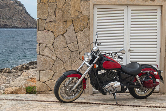 Rotes Cruiser-Motorrad geparkt vor Natursteinmauer an einer mediterranen Felsk&uuml;ste