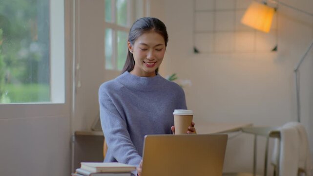 Work at home young asian woman working on laptop computer while sitting and hold coffee cup at home Morning lifestyle concept