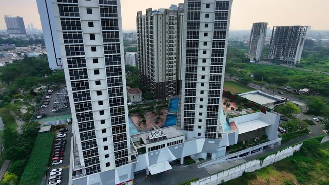 Cinematic aerial drone video tracking close to modern high-rise residential apartment towers with swimming pool podium facilities under a warm sunset sky