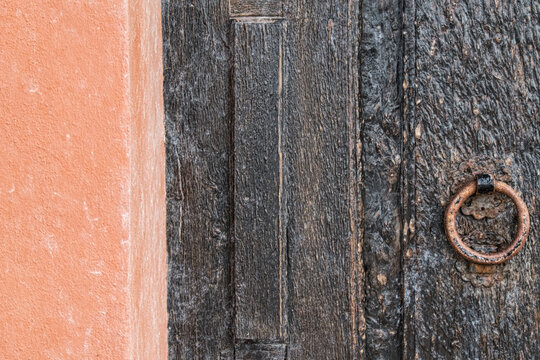 Detail einer alten verwitterten Holzt&uuml;r mit rostigem Eisenring neben terrakottafarbener Wand
