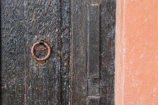 Detail einer alten verwitterten Holzt&uuml;r mit rostigem Eisenring neben terrakottafarbener Wand