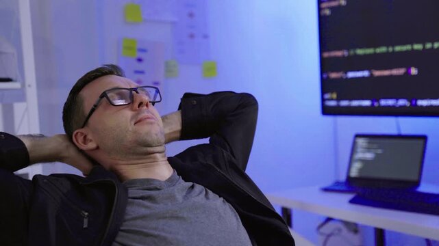 Tired programmer stretching arms at computer desk in office