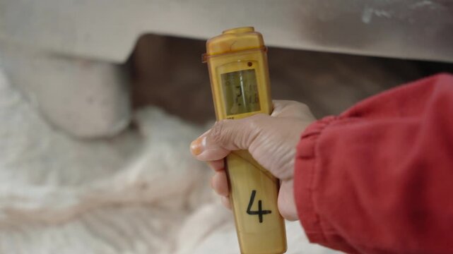 Gloved worker holds a digital probe thermometer to verify dough temperature during commercial mixing.
