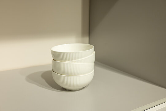 Stacked white ceramic bowls on neutral shelf in minimalist kitchen