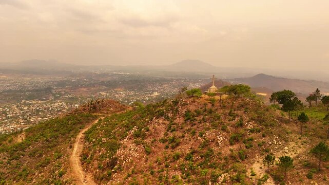 An aerial orbit circles the Way of the Cross monument on Michiru Mountain, revealing Blantyre through cloudy, whitish haze.