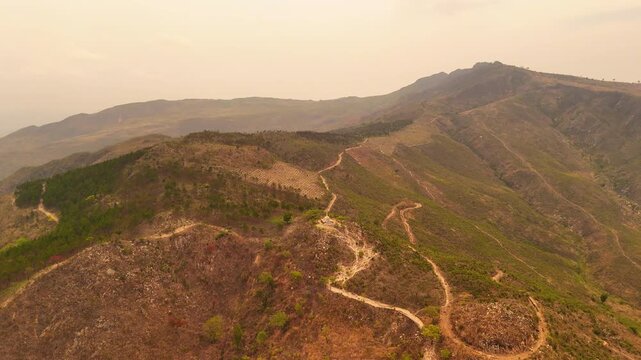 An aerial view shows the Way of the Cross trail, a hilltop cross, and paths continuing across the rugged slopes of Michiru Mountain.