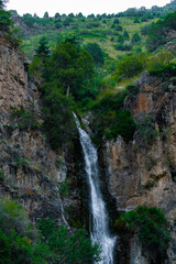 Obraz premium Beautiful vertical waterfall in the mountains. Powerful water stream flowing down the rocks background.