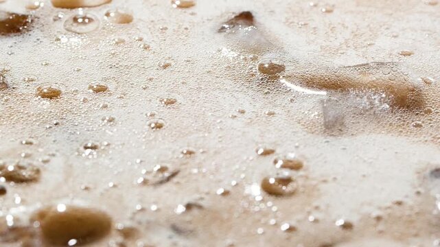 Slow motion closeup pouring cola with ice cubes and bubbles, soft drink top view