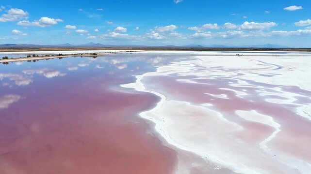 Aerial view of vibrant pink salt flats with white crystalline deposits under blue sky with scattered clouds