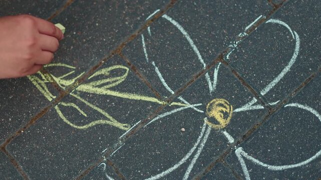 Woman drawing flower with green chalk on grey pavement. Creative outdoor activity during summer day. Artistic expression and sidewalk art play on stone surface.