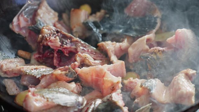 Close-up of fresh fish pieces and ginger slices quickly stir-fried in an iron pot