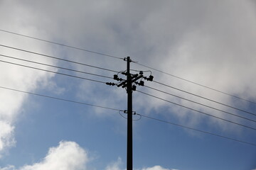 Obraz premium A utility pole stands against a blue sky with clouds.