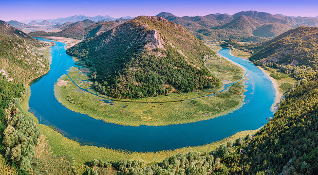 Crnojevic river creating a famous horseshoe bend, surrounded by lush green hills and aquatic vegetation under a clear sky