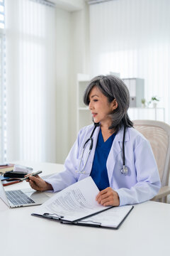 Doctor working in office, using a laptop to access patient records on system. Mature physician using modern technology in her practice.