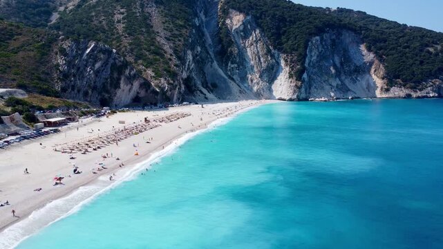Drone aerial footage of the crystal-clear turquoise waters and white pebble shoreline of Myrtos Beach in Kefalonia, Greece, captured on a sunny summer day.