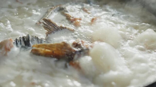 Close up shot of fish pieces rolling and boiling in thick white fish soup
