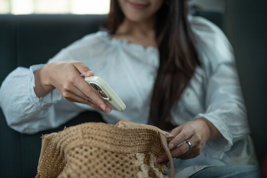 Close up of young Asian woman placing a smartphone into a woven handbag during a taxi cab car ride.