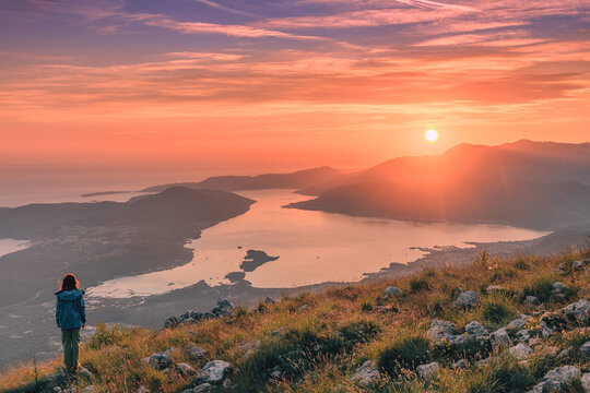 Woman standing on mountain top at sunset, looking across scenic bay and mountains, finding freedom and peace in nature