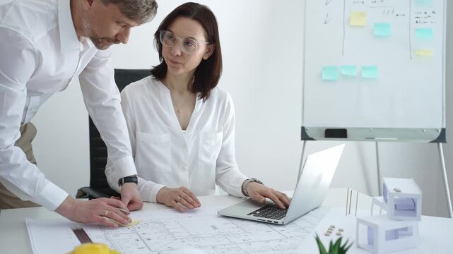 Architects collaborating on building design, reviewing blueprint plans and architectural models, creating detailed floor layout sketches in a professional office environment
