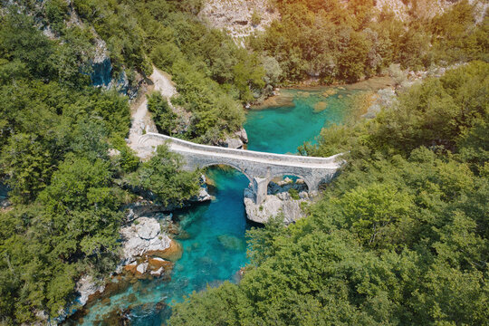 Ancient stone arch bridge crossing the turquoise waters of Mrtvica river in Montenegro, showcasing natural beauty and infrastructure