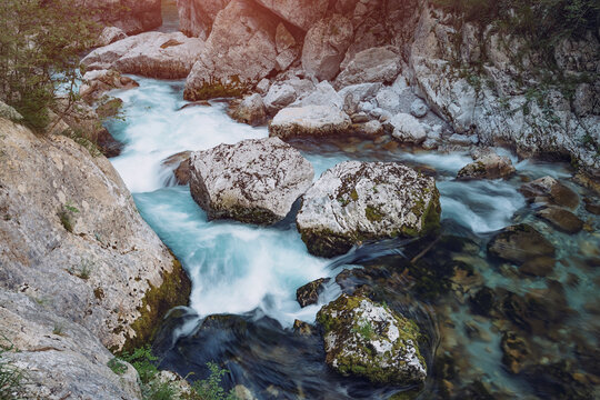 Clear river water swiftly flowing through a narrow mountain gorge, surrounded by lush green vegetation and ancient rock formations