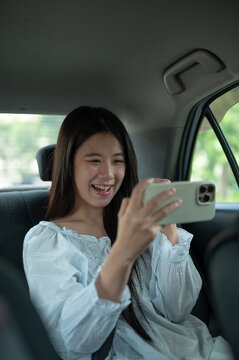 Young Asian woman enjoy watching media or cheering on smartphone in the back seat of a taxi cab car.