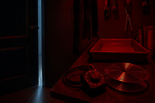 Coiled darkroom timer cable and empty stainless steel film reel in workstation corner, prepared practical brand campaign concept.