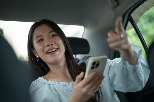 Young Asian woman giving a direction to driver while traveling in the back seat of a taxi cab car.