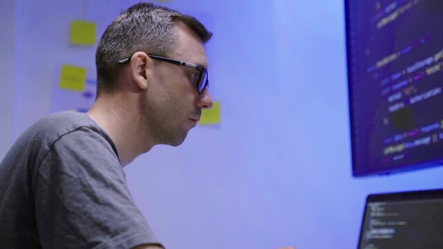 Software developer writing code on computer monitor in office