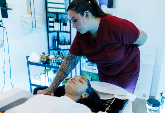 Hairdresser washing client's hair in modern salon basin
