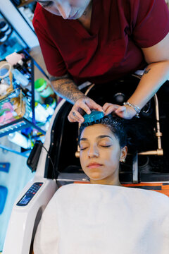 Hairdresser washing woman's hair with scalp massager
