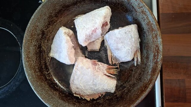 Flour-coated fish is fried in a pan