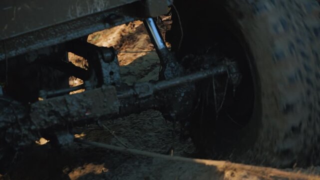 A low-angle close-up of a muddy SUV tire on a sandy surface. A winch cable is visible in the foreground. Warm sunlight highlights the extreme adventure and outdoor recreation